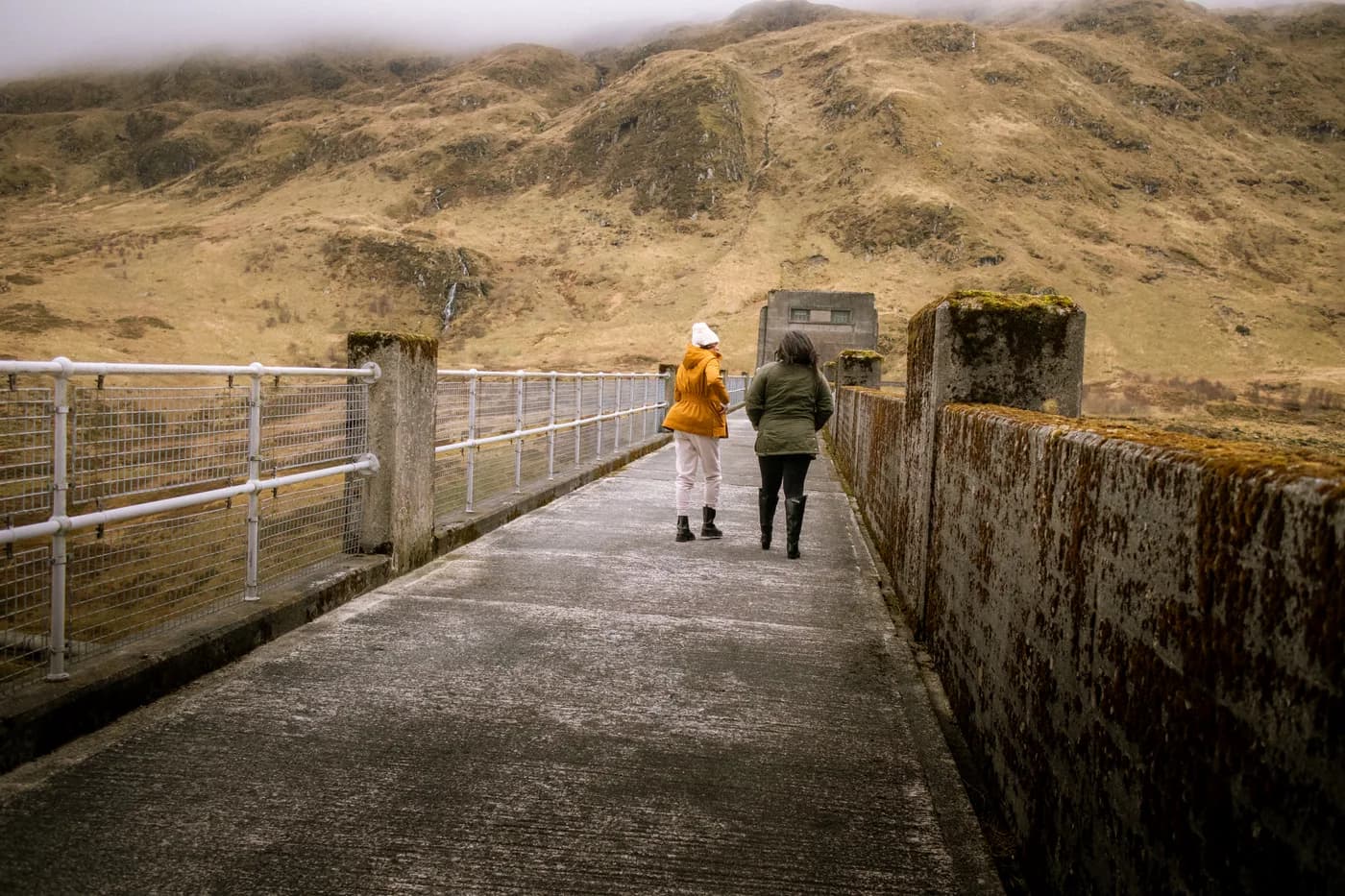 Allyson and her mum walking across a dam beneath Highland hills