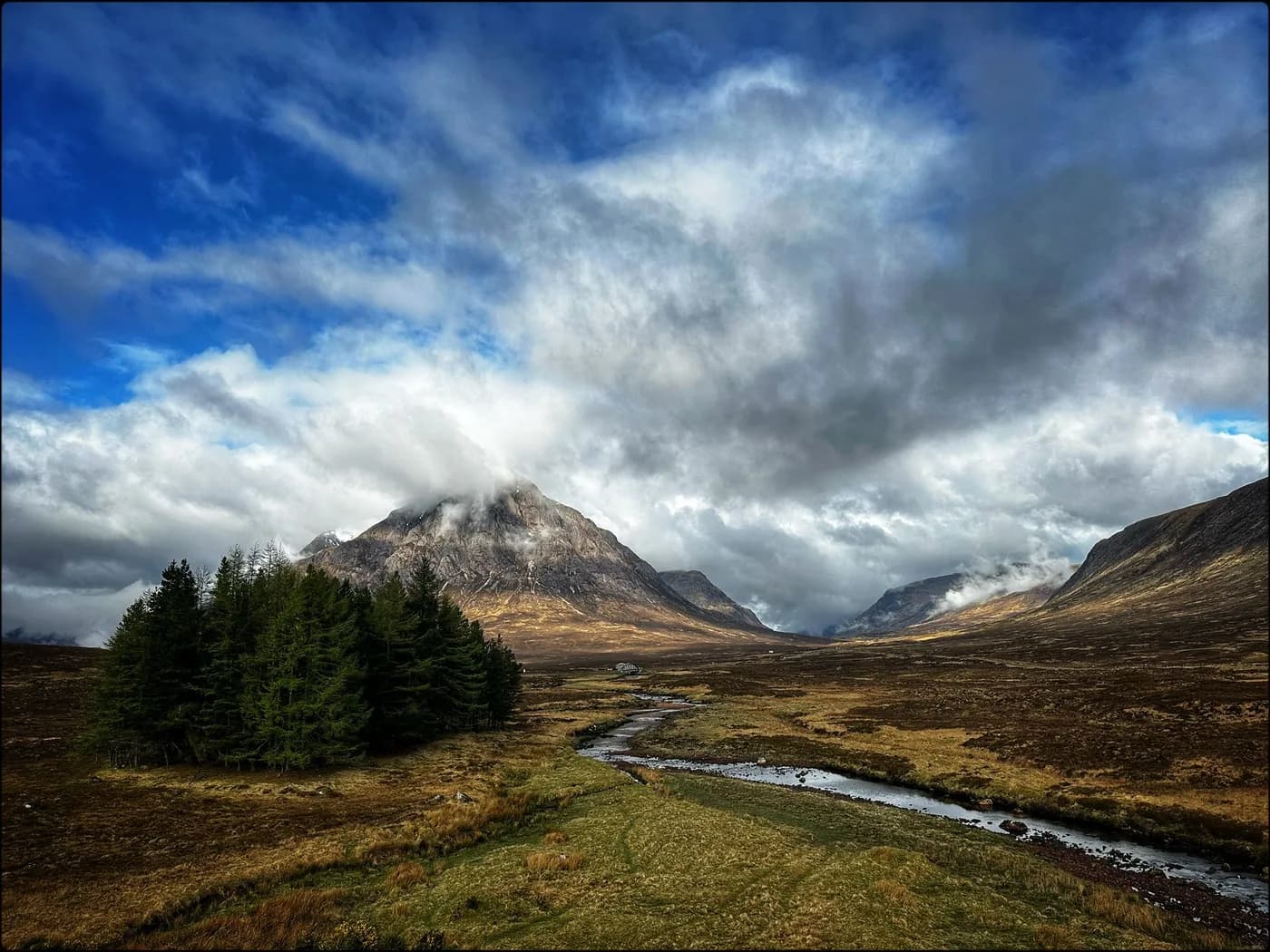 A river running through Glencoe beneath mountains and scattered clouds